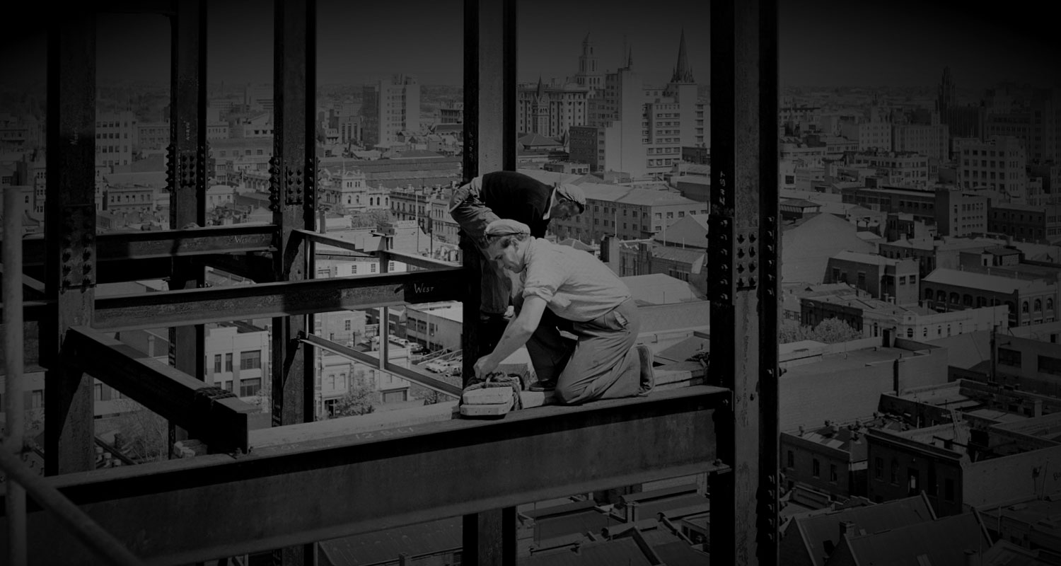 2 riggers on a steel girder with Melbourne city skyline behind and below them.