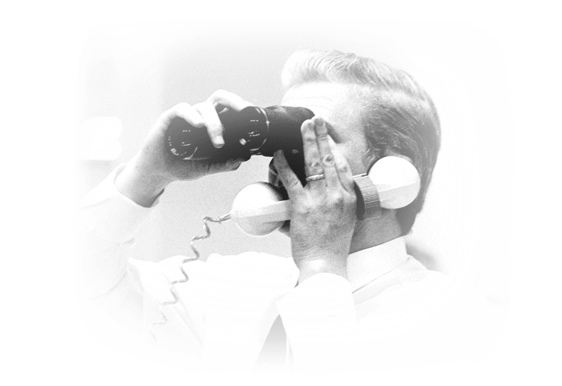 A man with a phone to his ear, looking through binoculars. 
