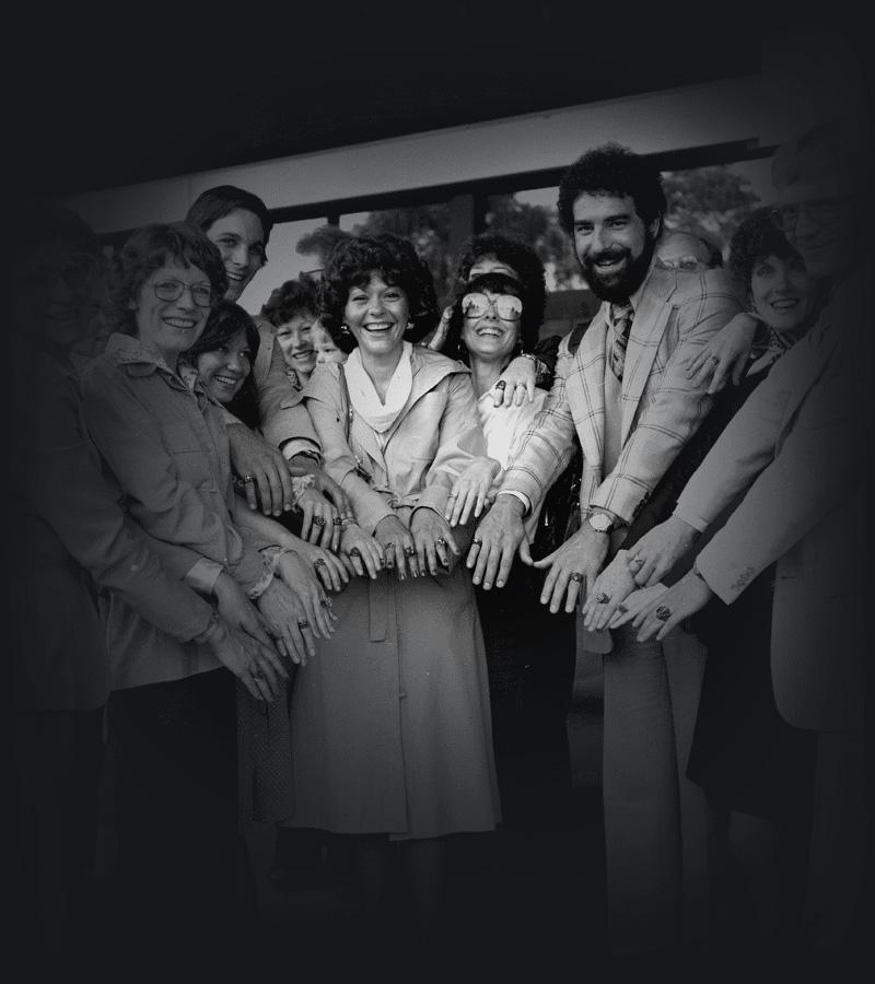 A group of men and women reaching their hands into the centre of the group and smiling. 