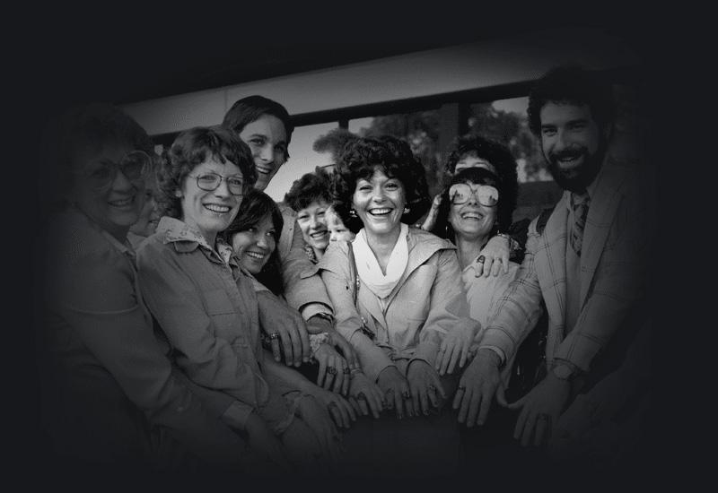 A group of men and women reaching their hands into the centre of the group and smiling. 
