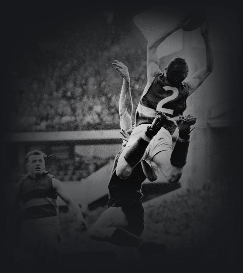 A footballer soars above his opponent to take a mark.
