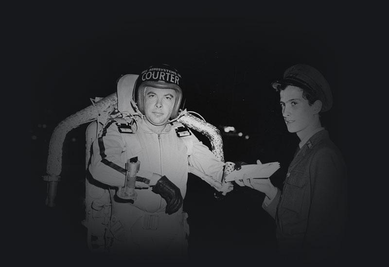 A postman handing letters to a man wearing a rocket pack suit