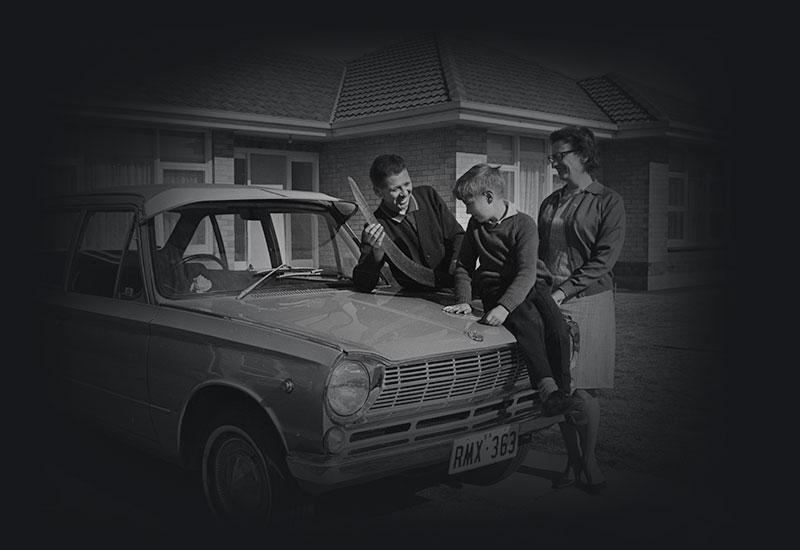 A young family stand on their driveway beside a car