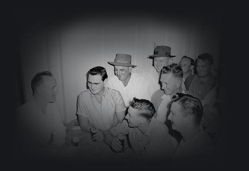 Men holding glasses of beer gathered at a bar.