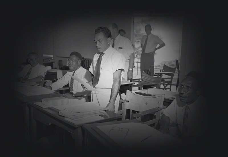 A Papuan Member, Mr Mahuru Rarua-Rarua, addressing the Papua and New Guinea Legislative Council at Port Moresby. To his left is a New Guinean Member, Mr Simogun Peta of the Sepik District, and on his right, Mr John Vuia, a prominent leader of the Tolai people in the Gazelle Peninsula area of New Britain