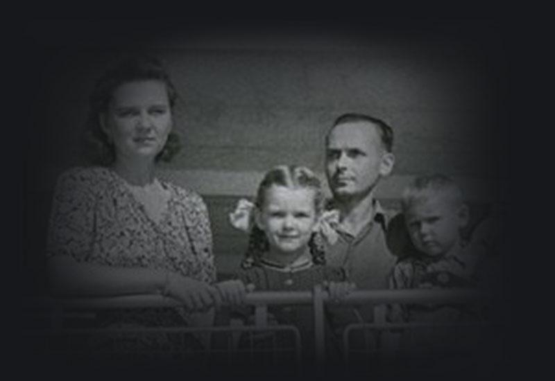 Maira Kalnins, wearing pigtails, standing at the ship's rail with her family. 