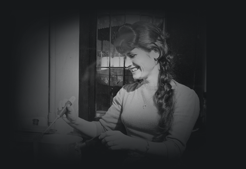 Vassiliki smiling and cooking on a gas stove.