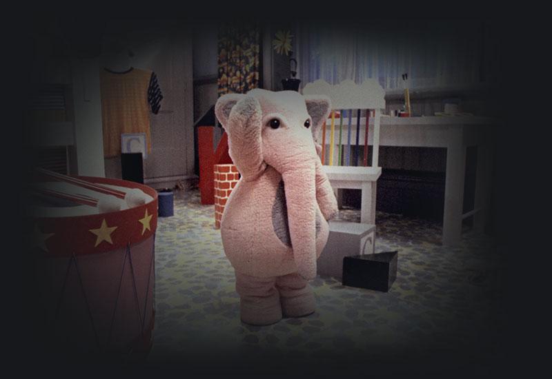 A person wearing a pink elephant costume amongst toys.