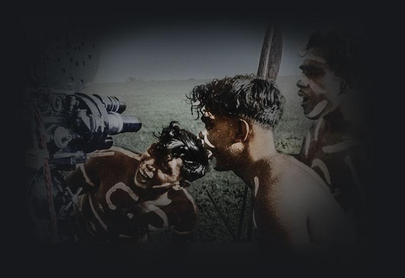 3 indigenous youths looking at a motion picture film camera.