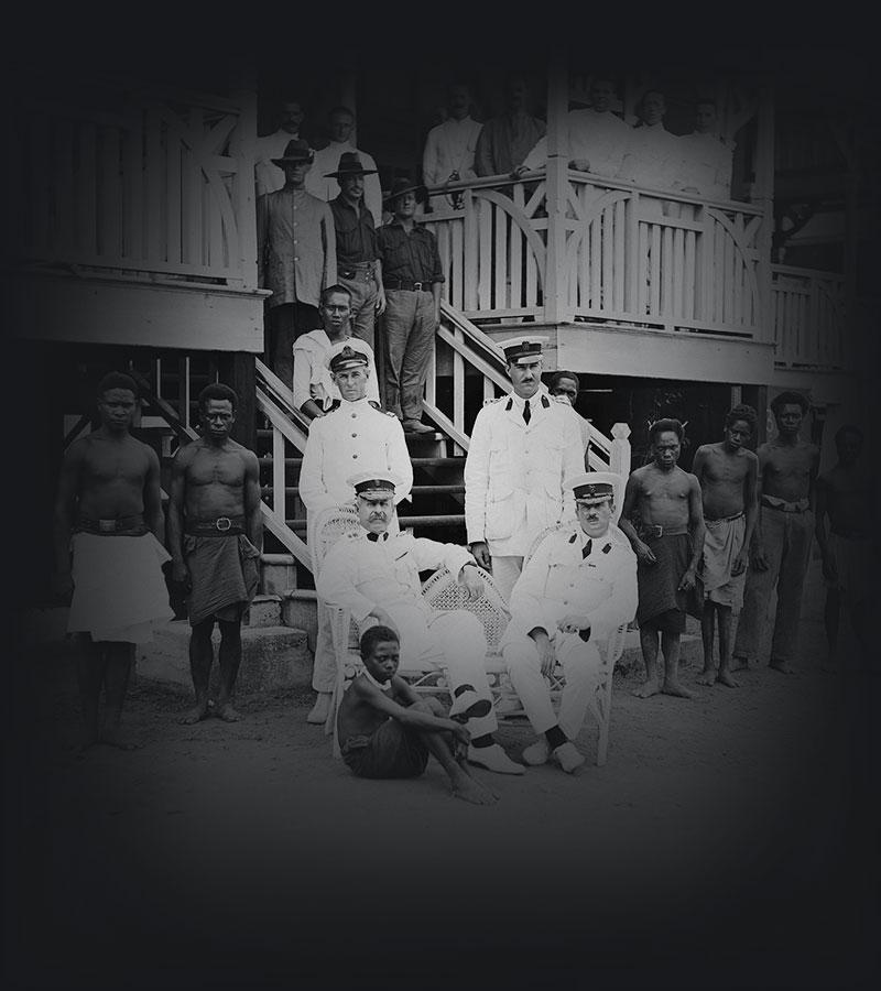 Army officers and Papua New Guinea staff at the entrance to a large timber building.