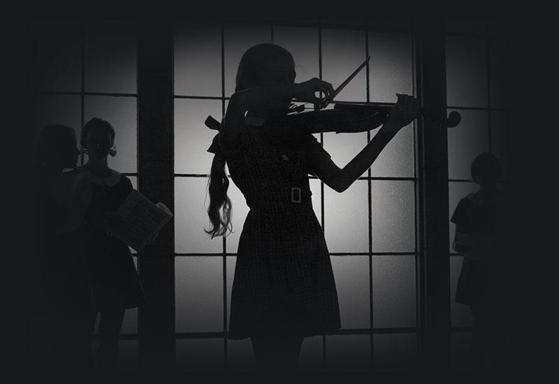 A young girl playing violin silhouetted before a window