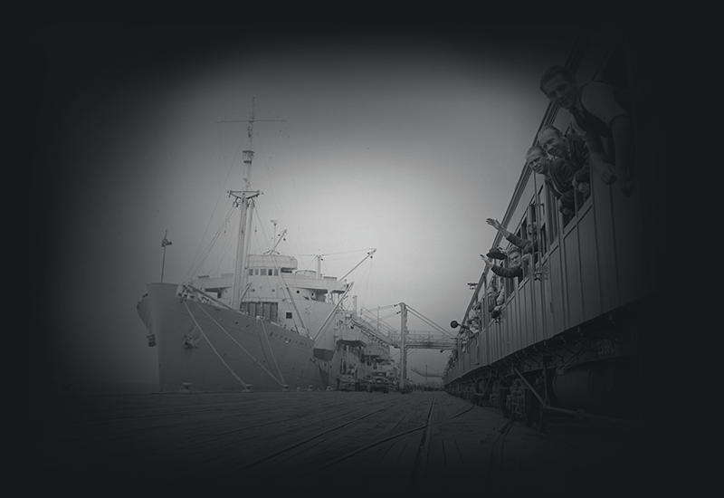 People waving from a train carriage on a dock beside a ship.