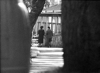 Black and white surveillance photograph of two people walking on a path.