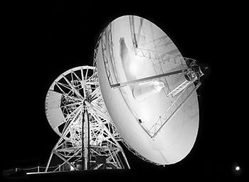 A large radio telescope illuminated at night.