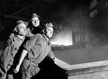 3 workers posing in helmets in a steel factory.