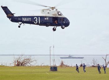 Blue and white helicopter Navy 31 lowering a crate onto grass.