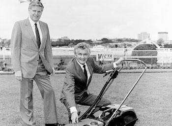 Men in suits beside a Victa lawn mower
