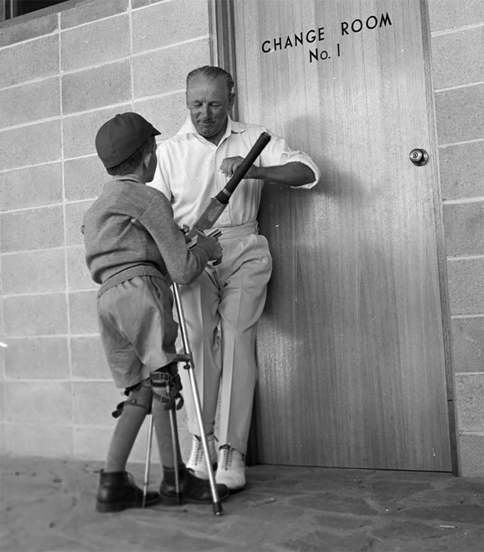 Sir Donald Bradman signing fan's cricket bat.