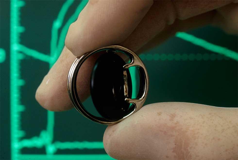 Artificial heart valve: pivoting disc surrounded by a thin metal exterior. It is held between gloved fingertips.