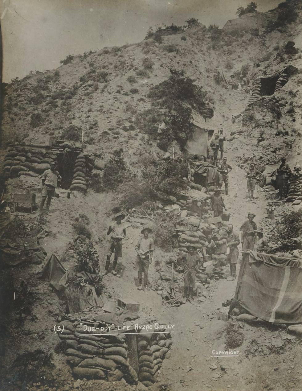 Men standing on a hillside in-font of the entrances to dugouts. 
