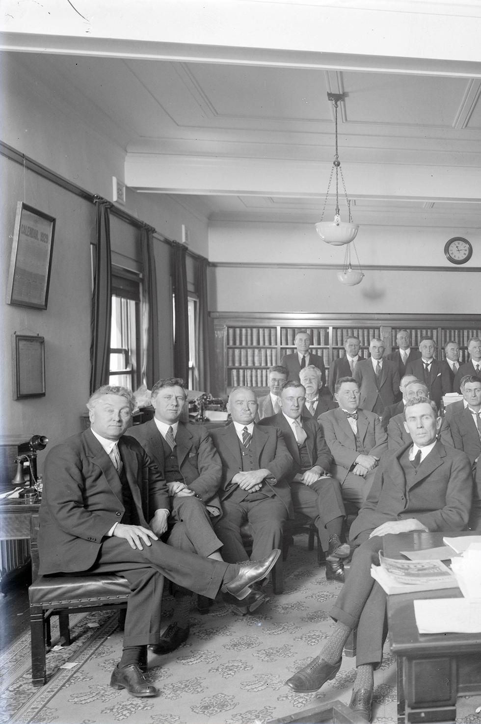 The Labor Caucus, assembled at Parliament House on 21 October 1929 to elect the members of the Cabinet of James Scullin. Neither Ben Chifley nor John Curtin (both seated at the desk) was included, but Joseph Lyons (seated left) was among the nine ministers elected. NAA: A3560, 6120