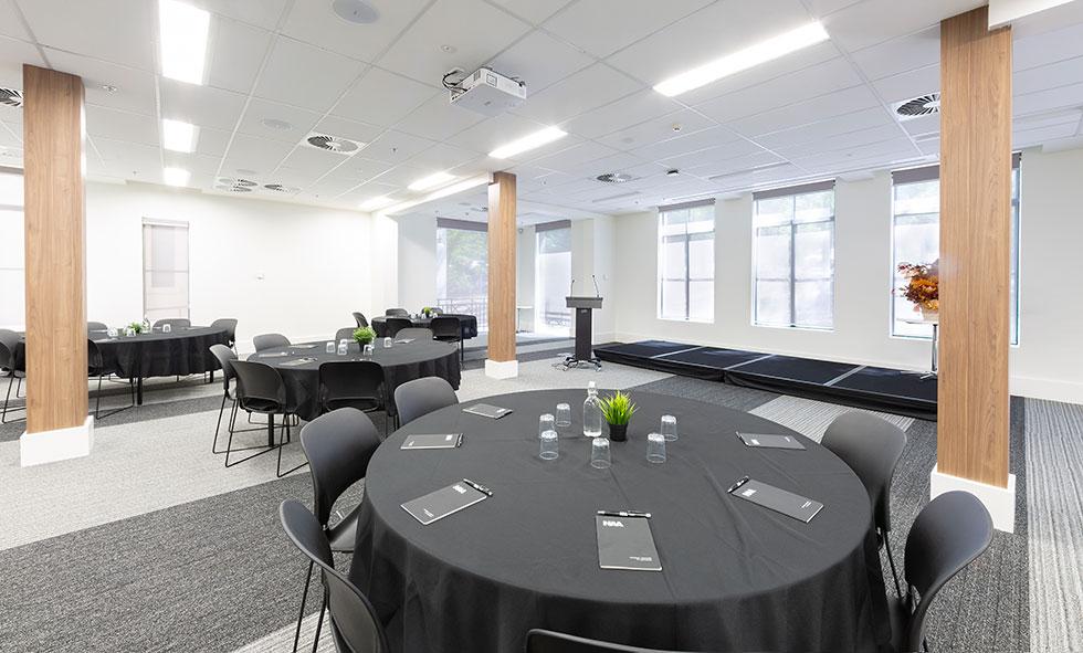Conference room showing round tables with black tablecloths and lectern.