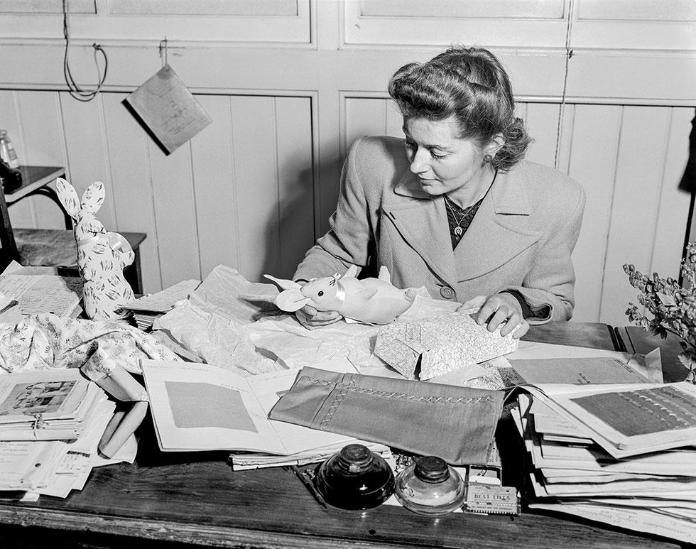 A woman sits at a desk covered with school work-books