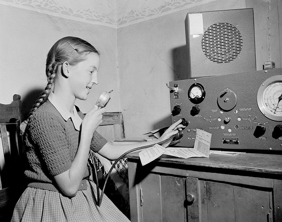 A young student speaking into a microphone attached to a large radio tranceiver.