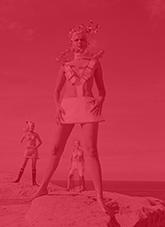 Three women standing on a sandstone cliff above the ocean dressed in futuristic fashion.