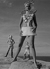 Three women standing on a sandstone cliff above the ocean dressed in futuristic fashion.