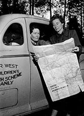 Sister Graves (left) and Fawcett of the New South Wales Far West Children's Health Scheme study the map to find an alternative route to an isolated settlement cut off by rain.