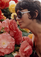 A woman in sunglasses smells a pink begonia.