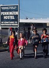 Children in bright coloured clothing walking along a drive way. Blue buildings behind them.