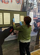 A conservator wearing gloves adjusting an exhibition document display