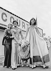 A model stands next to a sheep showcasing her wool fashion dress.