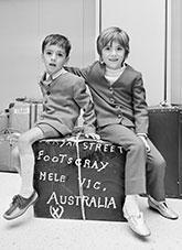 Two Maltese children sitting on a suitcase.