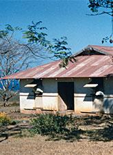 Hot climate house with window shades and faded red tin roof.