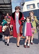 A woman with 5 children and their bags after disembarking from a ship.