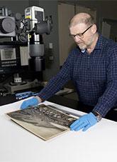 Conservator viewing an old photograph with gloved hands.