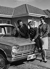 A young family stand on their driveway beside their car