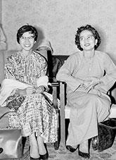 3 smiling women with short hair, wearing early 60s clothing, sitting on timber armchairs chairs.