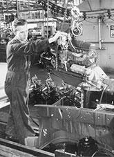 A man guiding an engine into tje engine bay of a car body on a production line.