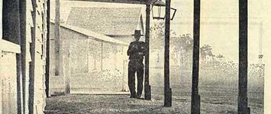 Man standing under a large verandah with dirt floor.