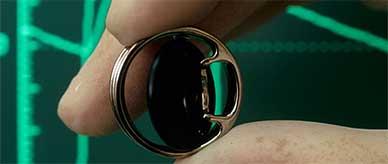 Artificial heart valve: pivoting disc surrounded by a thin metal exterior. It is held between gloved fingertips.