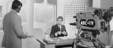 A man sitting at a desk infront of an ABC-TV camera.