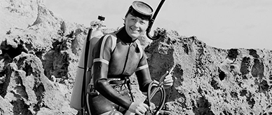 Scuba diver sitting on rocks with her speargun.