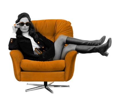 A woman wearing skirt-suit, boots and sunglasses reclining in a velour swivel chair
