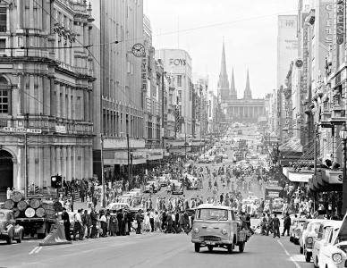 Pedestrians crossing Bourke Street in Melbourne. The Victorian Parliament and Saint Patricks Cathedral visible in the background.