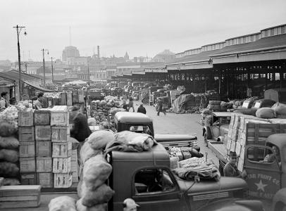 Boxes of fruit and vegetables on flat-bed trucks at a market.