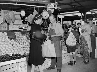 A fruit and vegetable grocer with shoppers at an open-air market.